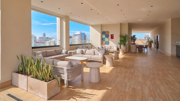 A spacious living area with a large sofa set, multiple seating options, and a view of the cityscape through large windows. - Niza City Tower Downtownsd Pool Gym Balcony (Santo Domingo)