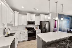 A modern kitchen with white cabinets, stainless steel appliances, and a bar area with stools.