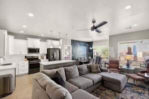 A modern kitchen with white cabinets, a microwave, and a stove. There is a dining area with a table and chairs.