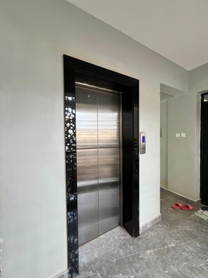 Um elevador moderno com acabamento metálico, moldura preta e painel de controle à direita.