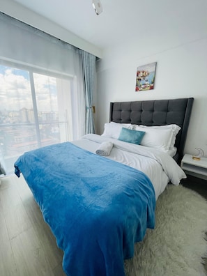Quarto com cama grande, vista da cidade, um quadro na parede e um tapete felpudo.