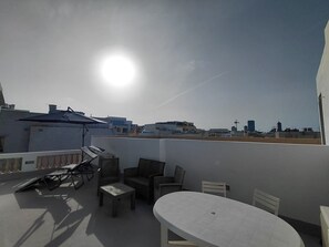 Eine Dachterrasse mit Tisch und Stühlen, Sonnenschirm und Blick auf die Skyline der Stadt.