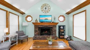 A living room with a fireplace, a television, and a clock on the wall. - Beach Oasis, 4BR, Sleeps 12, Mins to Arrowhead (Raytown)