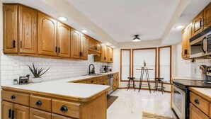 A kitchen with wooden cabinets, white countertops, a central island, a stove, and a microwave. - Beach Oasis, 4BR, Sleeps 12, Mins to Arrowhead (Raytown)