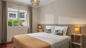 Une chambre d’hôtel avec un lit, deux lampes de chevet, une fenêtre avec des rideaux et une vue sur les bâtiments environnants.