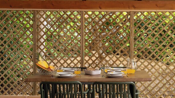 Une table en bois, dressée pour le petit-déjeuner, avec un décor en treillis en arrière-plan.