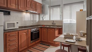 Une cuisine dotée de meubles en bois, d’un four à micro-ondes, d’un four traditionnel, d’un évier et d’un coin repas avec des chaises et une table.