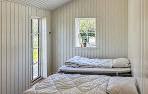 Een kamer met twee bedden, een raam met uitzicht op groen en een kleine plant op de vensterbank.