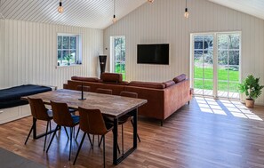 Een modern interieur met een houten eettafel, een bruine leren bank en een aan de muur bevestigde televisie.