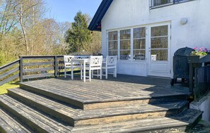A wooden deck with a table and chairs, a covered area with flowers, and a white building with large windows. - Awesome home in Tisvildeleje with WiFi (Tisvildeleje)