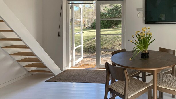 Un comedor con una mesa redonda, sillas, una planta en maceta y una escalera que conduce a una puerta de cristal.