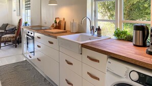 Una cocina moderna con encimera de madera, armarios blancos, lavadora integrada y vistas al exterior.
