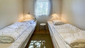 Eine kleine, einfache Unterkunft mit zwei Betten, einem Fenster mit Vorhängen und einem kleinen Tisch.