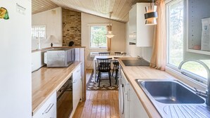 Eine kleine Küche mit Holzboden, weißen Schränken, einer eingebauten Mikrowelle, einem Spülbecken und einem Fenster mit Vorhängen.