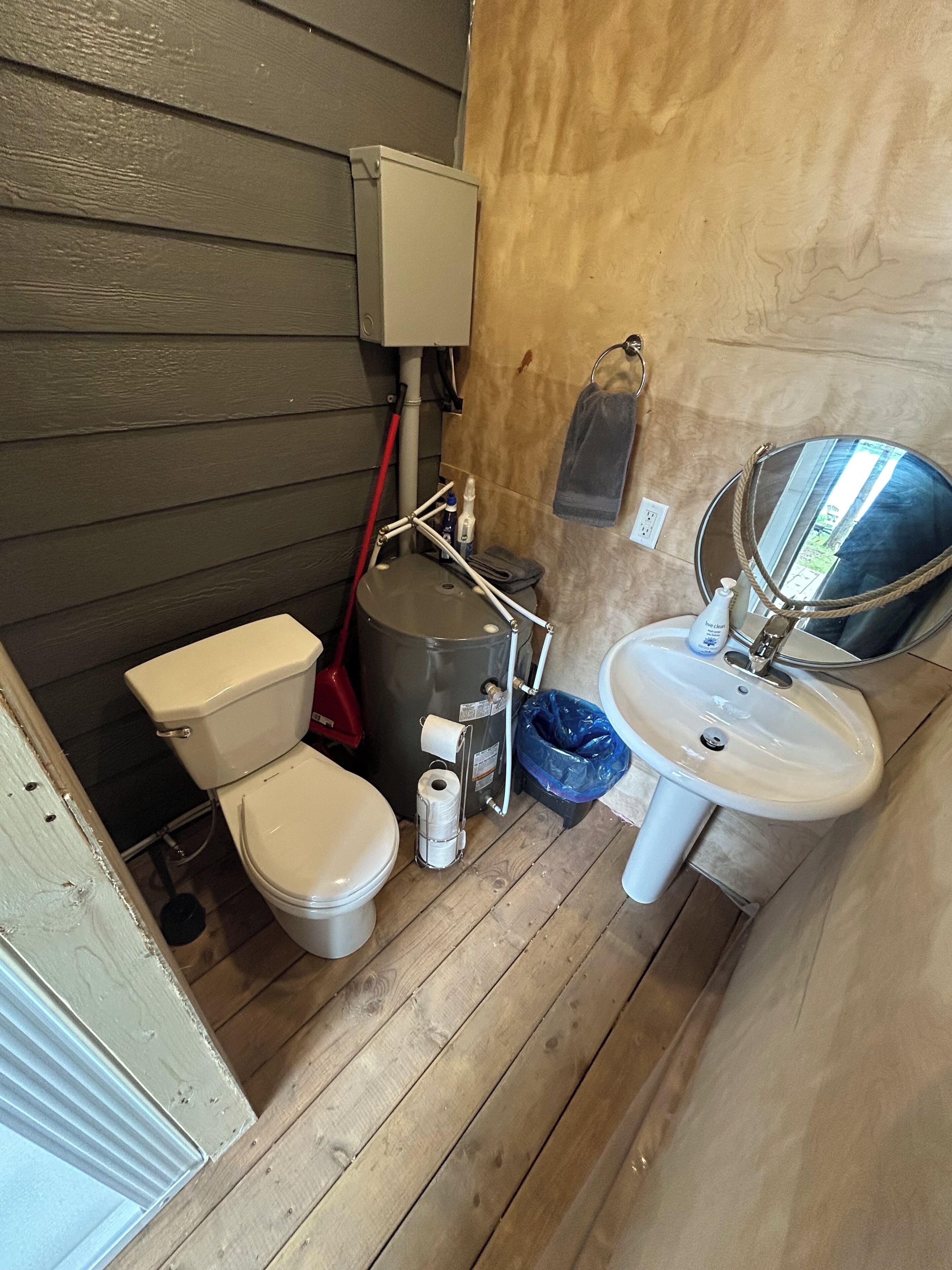 A compact bathroom with a toilet, a sink, a large water heater, and a mirror.