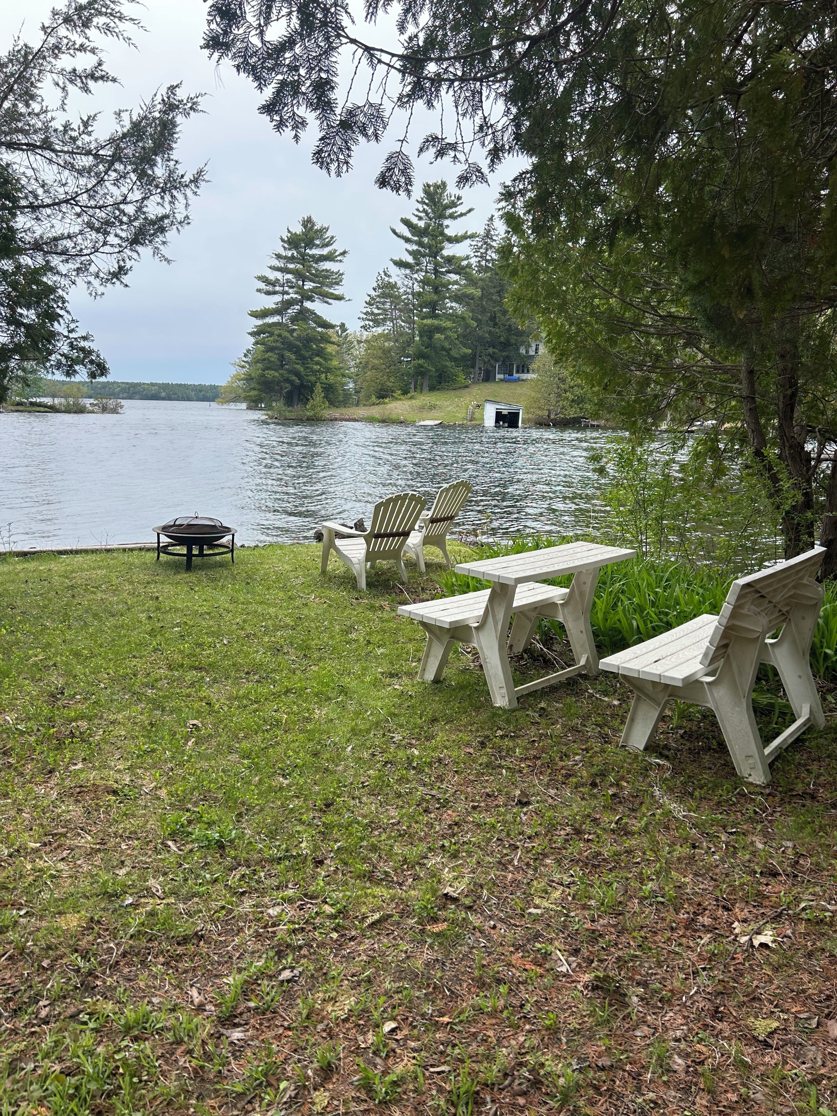 A lakeside setting with a picnic table and chairs, a grill, and a shed.