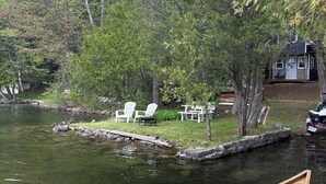 A wooden canoe docked at a riverside dock with a house and outdoor seating area in the background. - Lakefront Cabin on The Big Rideau (Rideau Lakes)