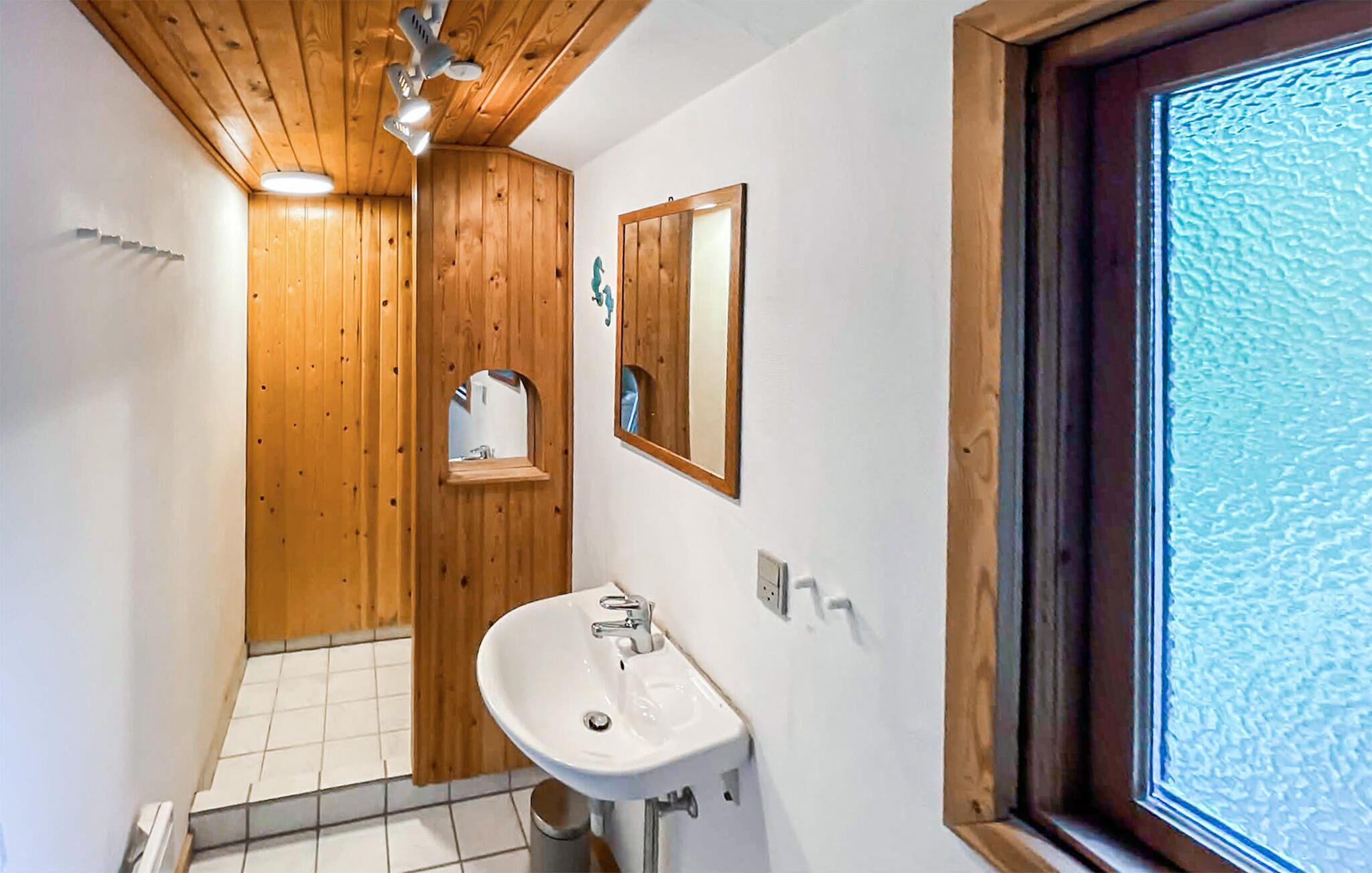Une salle de bain avec des murs en bois, un lavabo blanc, un miroir et une fenêtre offrant une vue intéressante.