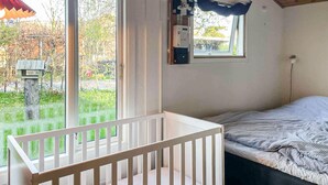 Una habitación con una cuna, una cama con ropa de cama a rayas, una ventana con cortina y vistas al exterior.