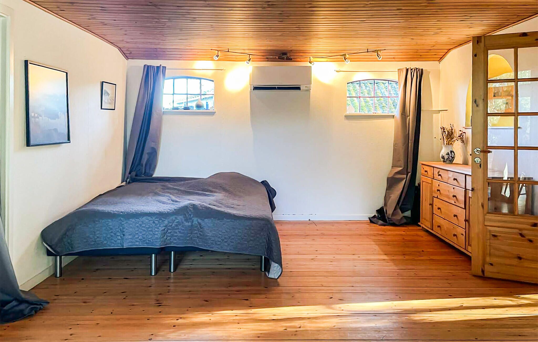 A bedroom with a bed, wooden floor, a dresser, and two windows.