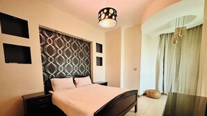A bedroom with a bed, bedside tables, a patterned headboard, a hanging light fixture, a mirror, and a window with curtains. - 02 BR apartment with full roof sea view (Red Sea Governorate)
