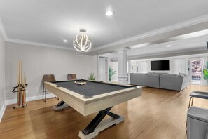 A pool table in a living room with a sofa and TV in the background.
