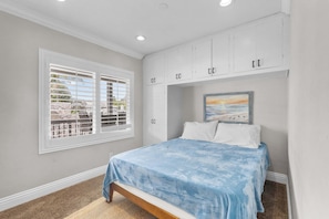 A bedroom with a bed, a window with blinds, a painting, and a built-in wardrobe.