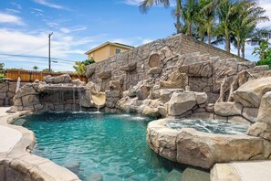 A pool with clear water, surrounded by large rocks and a waterfall feature. - LA Harbor 5BR | Water Slide, Hot Tub & Games | C&C (Los Angeles)