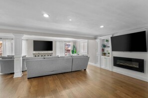 A modern living room with a grey sectional sofa, a flat-screen TV, a fireplace, and wooden flooring.