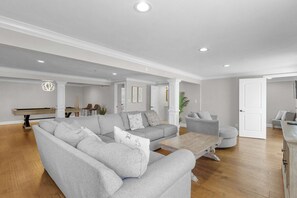 Una sala de estar con un sofá seccional gris, una mesa de centro de madera y una mesa de billar.