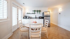 A modern kitchen with white cabinetry, a stainless steel refrigerator, and a dining area with a round table and white chairs.