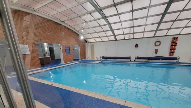 Piscina interna con pavimento piastrellato, parete in vetro e soffitto con struttura metallica.
