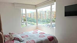 Una camera da letto con una grande finestra, un letto con biancheria a motivi e una TV a schermo piatto fissata al muro.