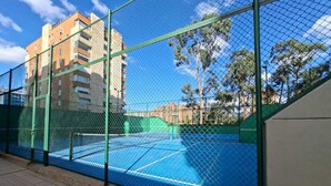 Un campo da tennis circondato da una recinzione verde, con un edificio sullo sfondo.
