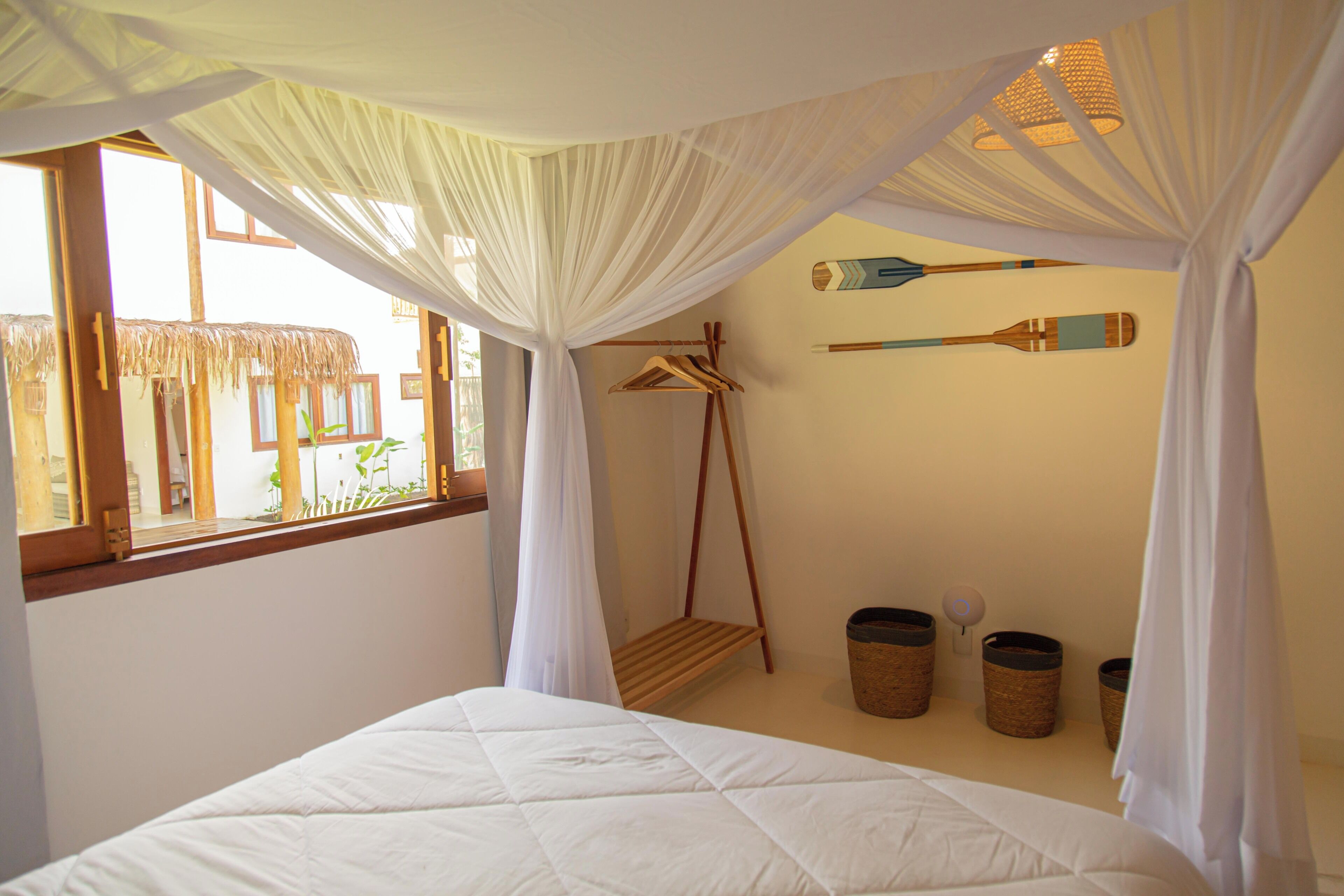 Une chambre avec un lit, une fenêtre donnant sur un beau paysage, un fauteuil suspendu et une pagaie fixée au mur.