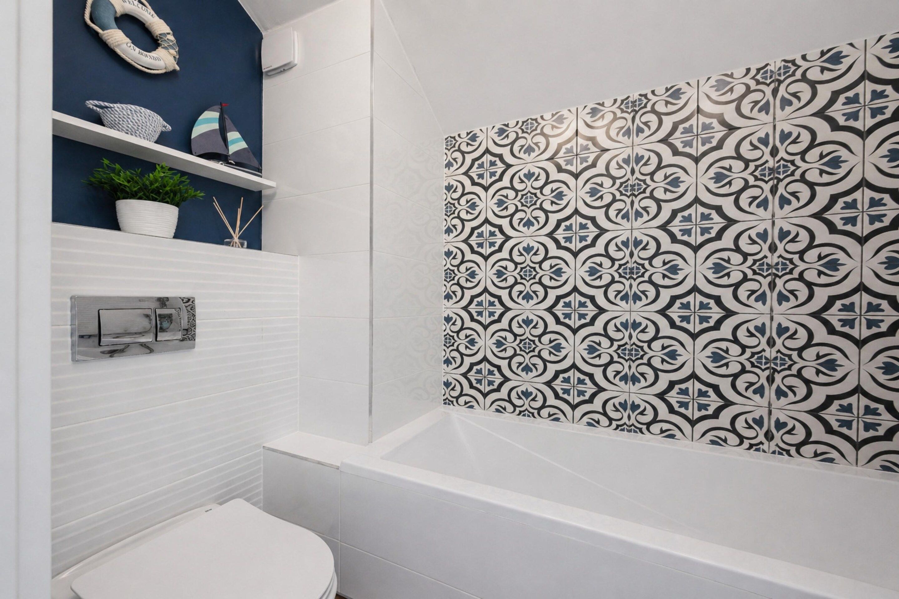 A bathroom with a white toilet, a white bathtub, and a wall with a black and white patterned tile design.