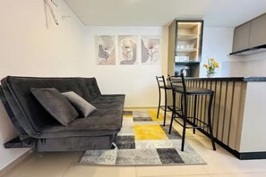 Ein moderner Wohnraum mit einer Couch, einer Küchenzeile mit Barhocker und abstrakter Wandkunst.