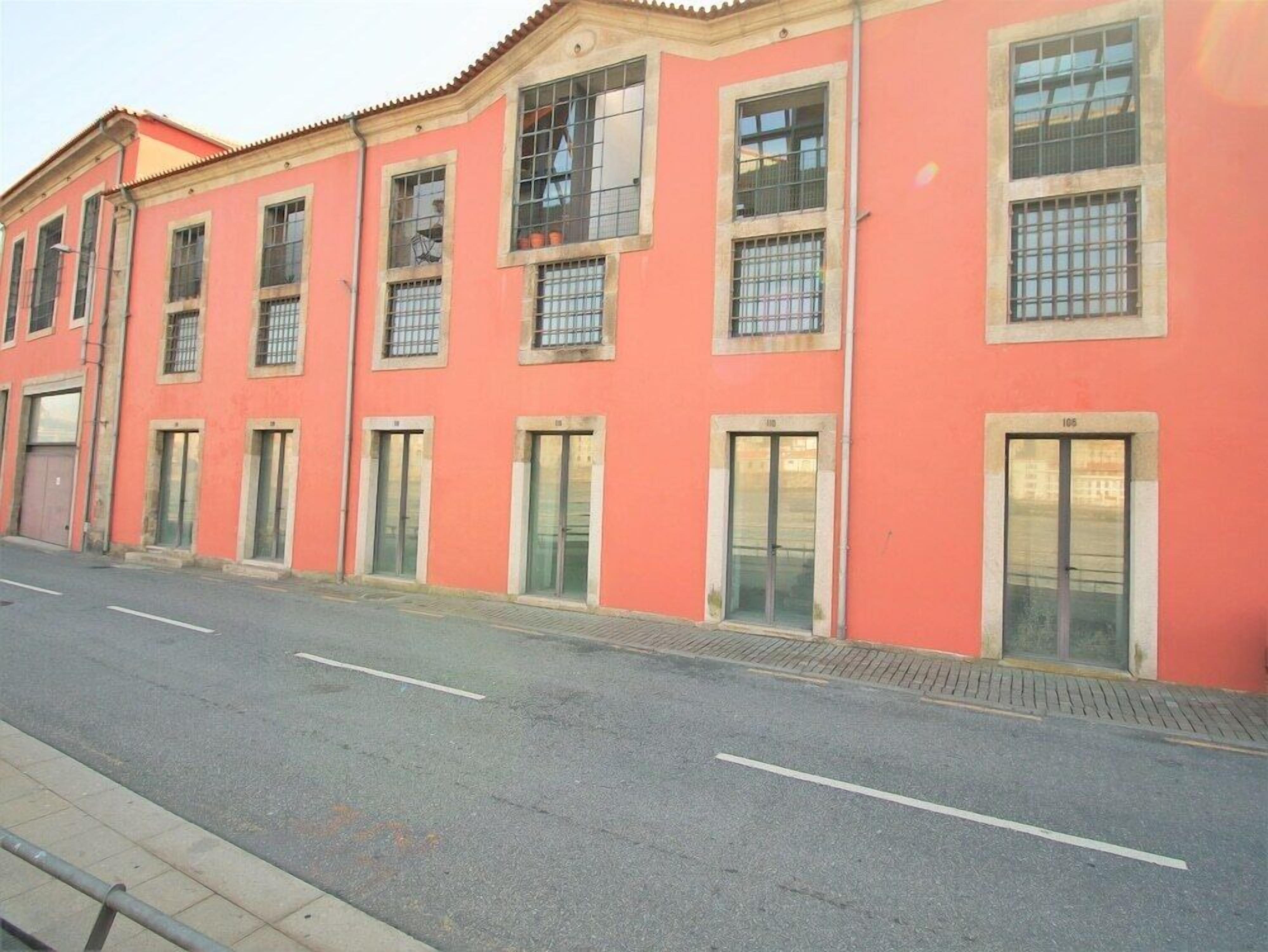 A row of pink buildings with multiple windows and doors, a clear road in front, and a sidewalk.