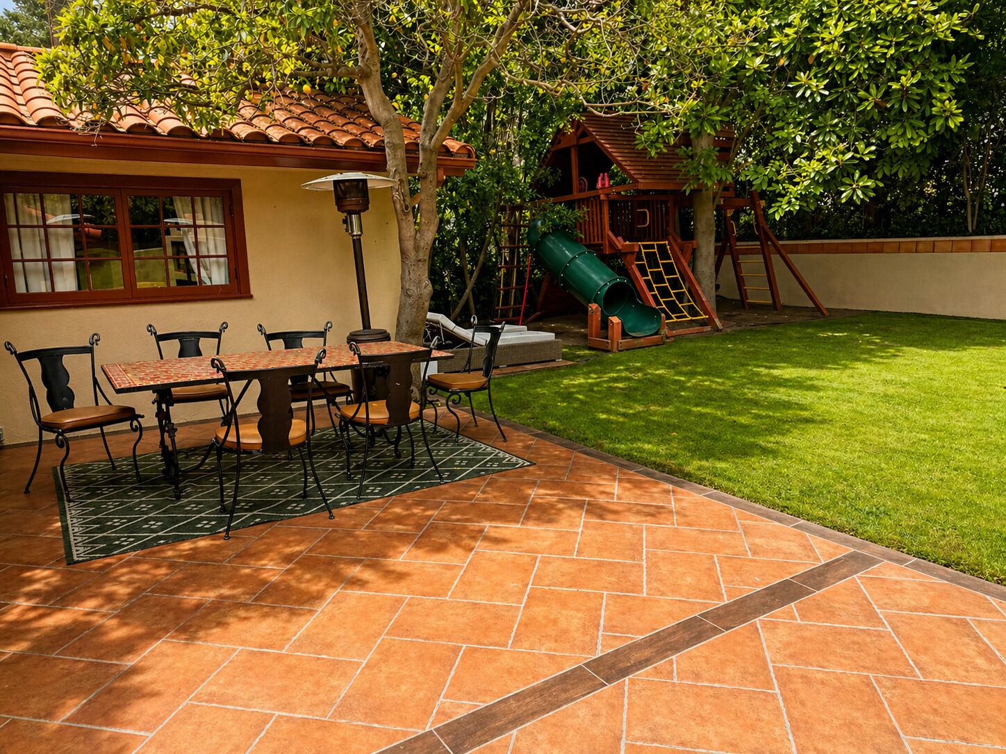 A patio with a table and chairs, a play structure, and a lawn.