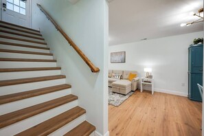 Eine Treppe mit Holzstufen und Geländer, ein Wohnzimmer mit Sofa, einem kleinen Tisch und einem Schrank.