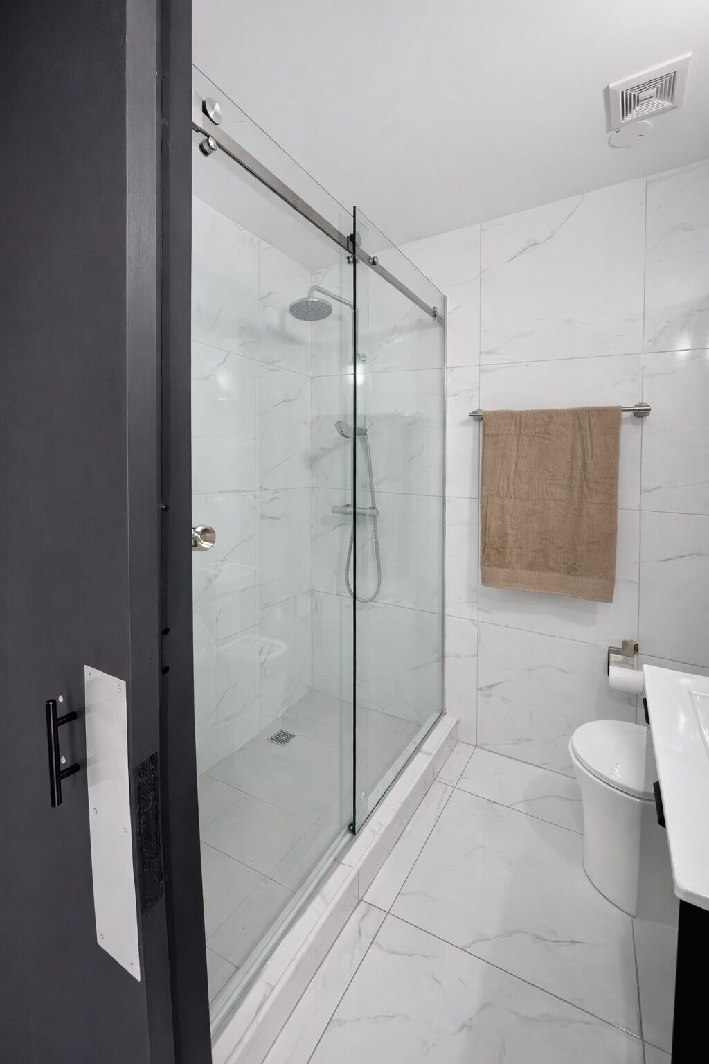 Un baño moderno con ducha de vidrio, azulejos de mármol blanco, inodoro blanco y barra para toallas.