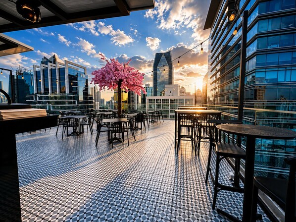 En tagterrasse med borde og stole, et pyntetræ og udsigt over bybilledet.