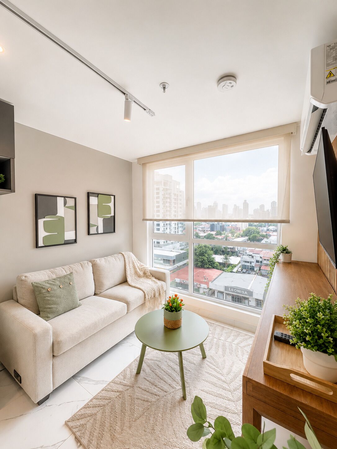 A modern living room with a sofa, a coffee table, and a view of a cityscape through large windows.