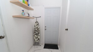 Um corredor estreito com uma porta branca, um tapete de entrada preto e um centro de passar roupa fixado na parede.