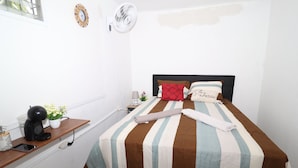 Uma cama bem arrumada com roupa de cama listrada, uma mesa de cabeceira com uma cafeteira, um relógio e um pequeno vaso de planta.