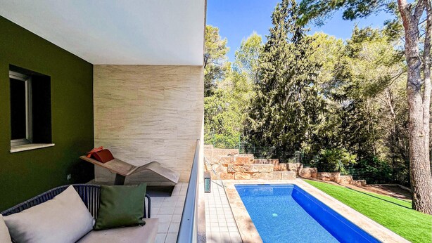 Ein moderner Außenbereich mit Pool, einer Steinmauer und einem grünen Rasen.