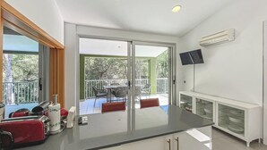 Eine moderne Küche mit einer großen Kochinsel, einem Essbereich mit Stühlen, einem an der Wand montierten Fernseher und einer Klimaanlage.