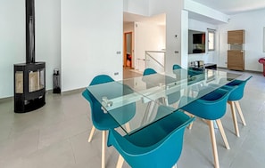 A modern dining area with a glass table and teal chairs, a black wood-burning stove, and a kitchen in the background. - Cozy home in Bonaire with private swimming pool, can be inside or outside (Bonaire)
