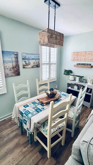 A dining area with a table set for four, surrounded by wooden chairs. A hanging light fixture is above the table, and there are two paintings on the wall. - Steps2White Sandy beach/Familyfun/fishing/Games (Gulfport)