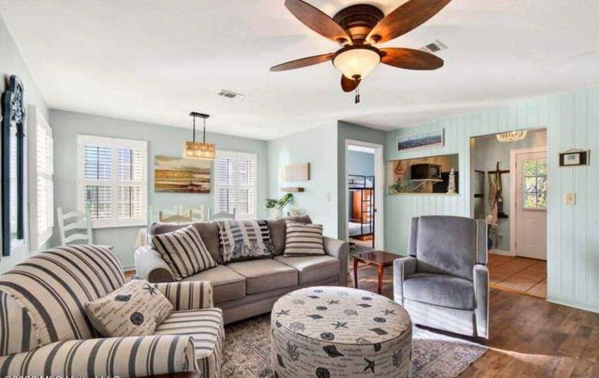 A living room with a ceiling fan, a sofa set, a round ottoman, and a chair.